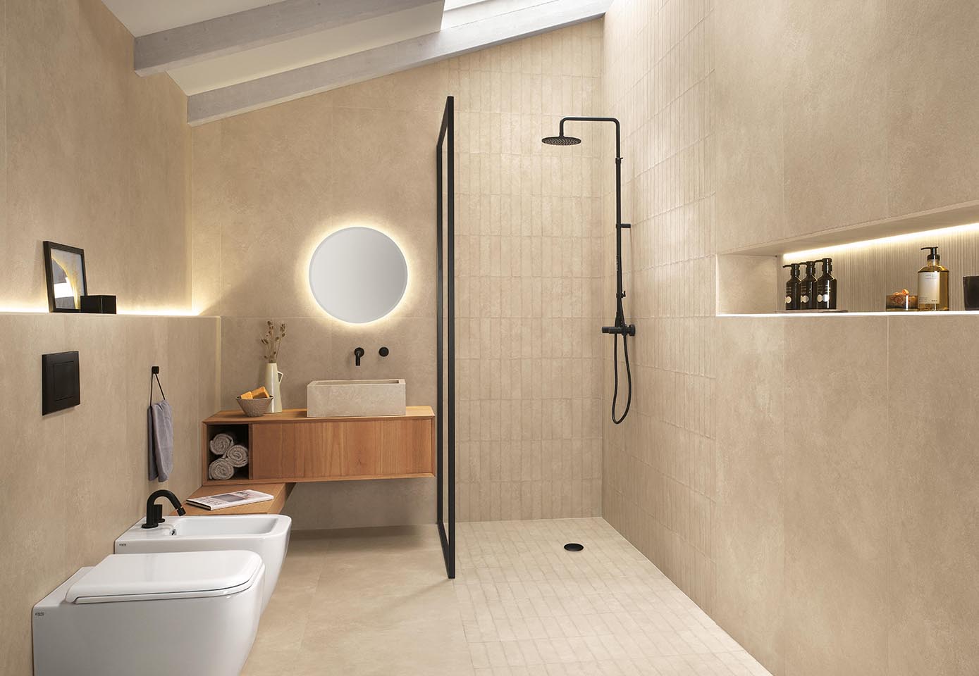 Bathroom with beige stone effect floor and wall tiles, countertop washbasin, wooden furniture and walk-in shower with matt black fittings.