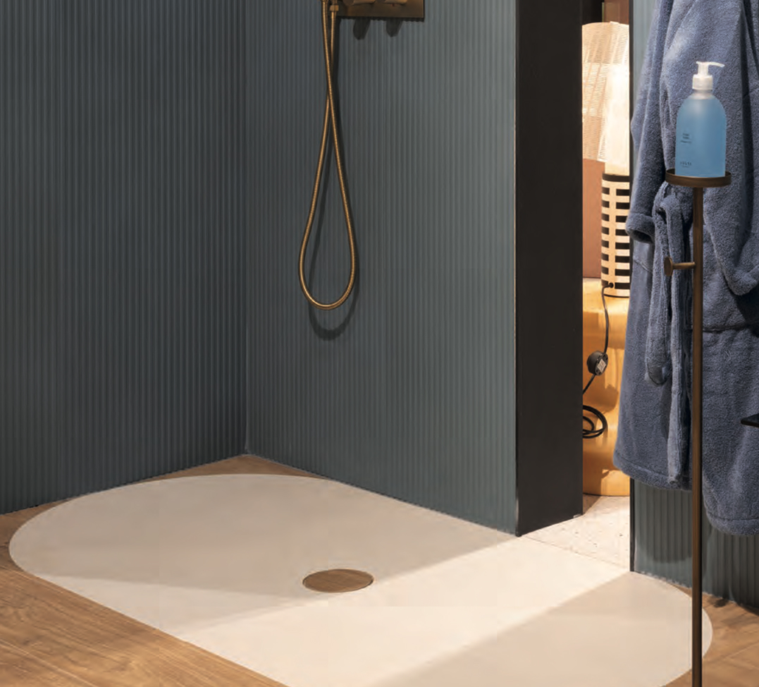 Light-coloured semi-circular shower tray with matt blue cladding and gold taps, next to a metal towel rail.