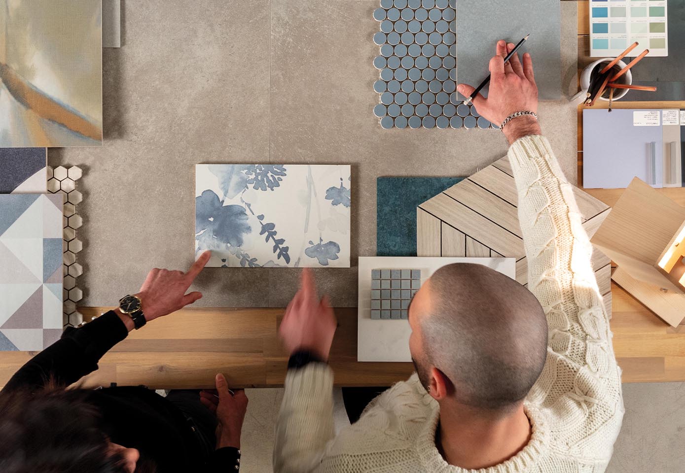 Designer at work on table with different tiles and stone effect moodboard in blue, grey, light blue, material inspirations and palette in cold tones.