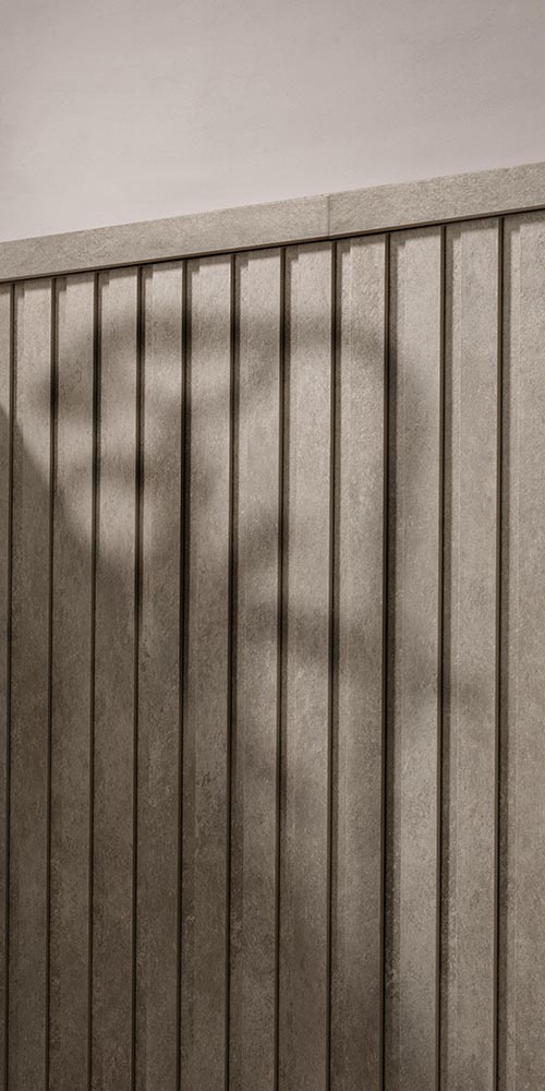 Detail of stoneware wall with dove-coloured vertical slats and material finish, lit by soft natural light.