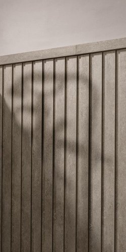 Détail d'un mur en grès avec des lattes verticales de couleur tourterelle et une finition matérielle, éclairé par une douce lumière naturelle.