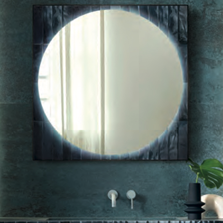 Round mirror framed by glossy blue tiles on a powder blue textured wall, with white washbasin and mixer tap.