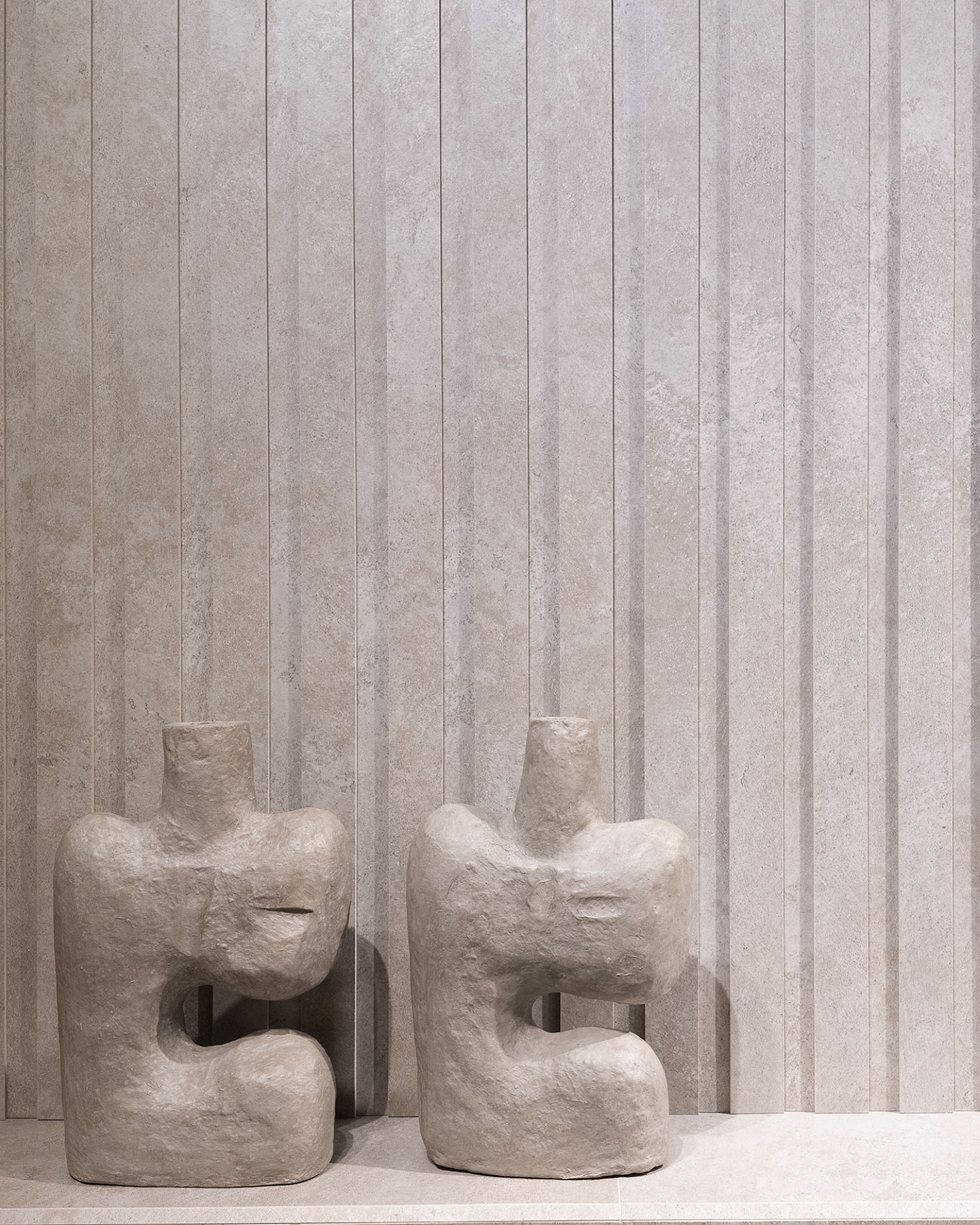 Beige ceramic cladding with a textured finish and vertical strips, two contrasting abstract sculptures in light stone.