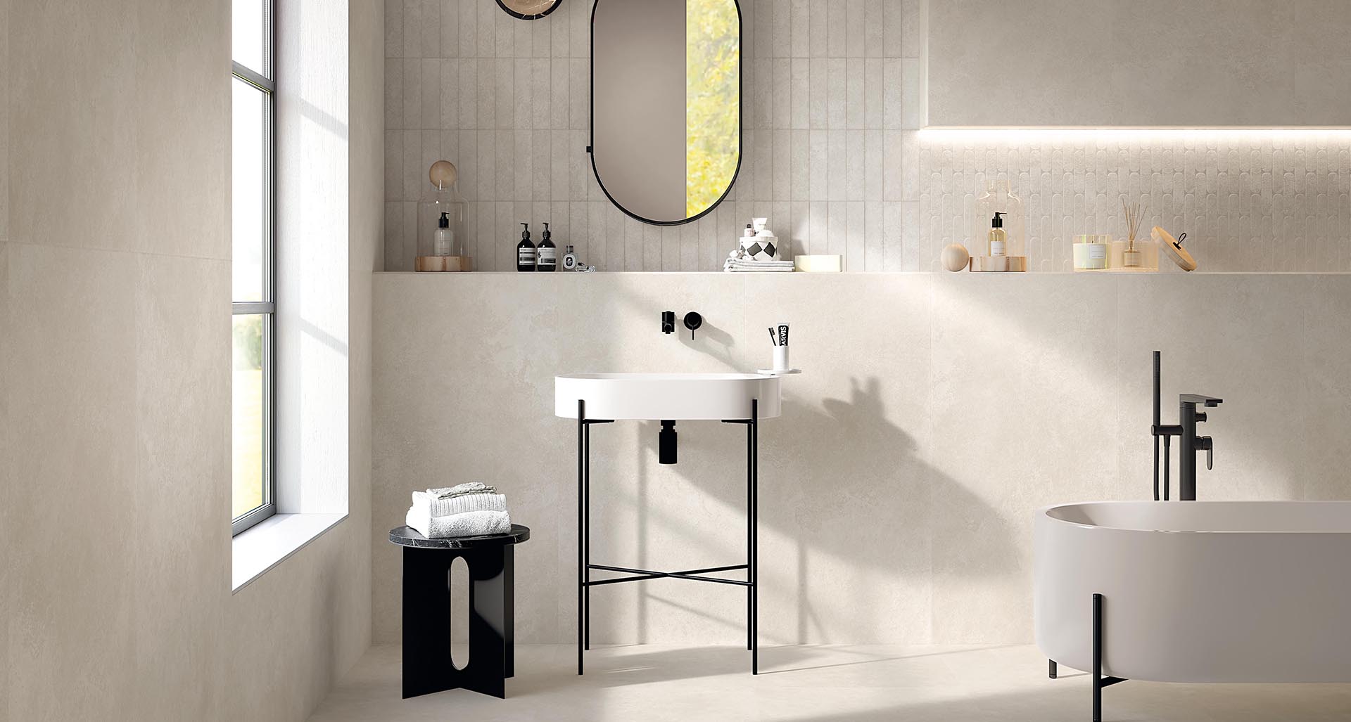 Bright bathroom with stone-effect beige floor and wall tiles, designer washbasin and bathtub with black taps.