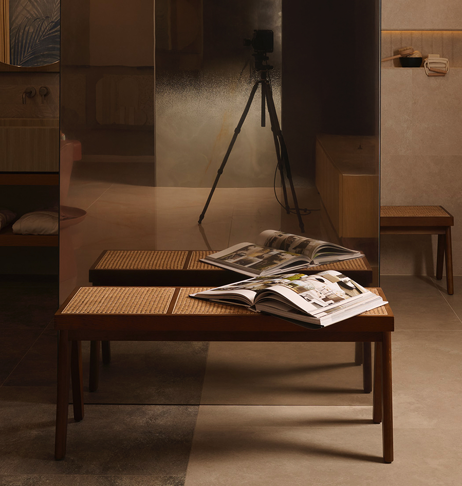 Slab with a shaded mirror effect reflects a wooden bench with open magazines, on a stone-effect ceramic floor.