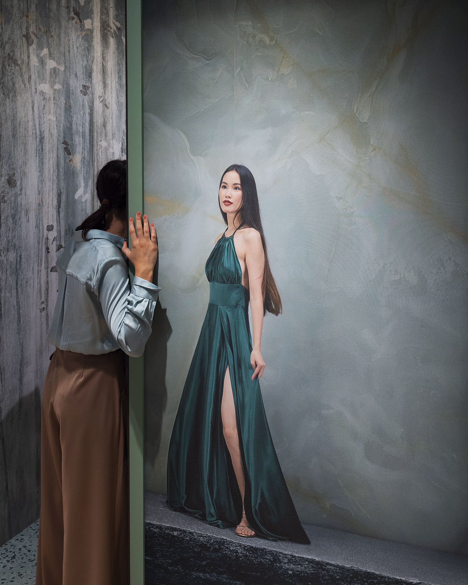 Installation with large green onyx-effect ceramic slabs and a full-height print of a female figure in an emerald green dress.
