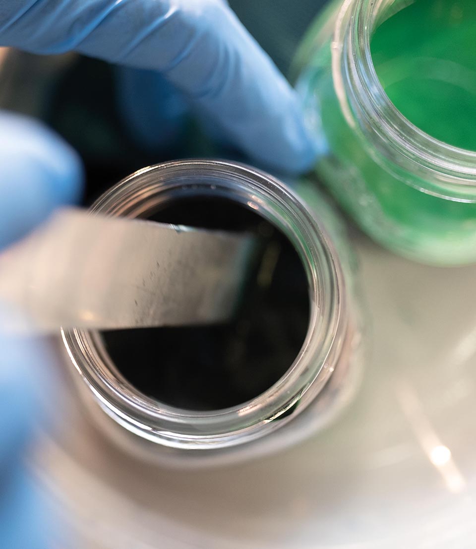 Detail of ceramic pigments in jar, manually processed with spatula in laboratory, in green and black shades.
