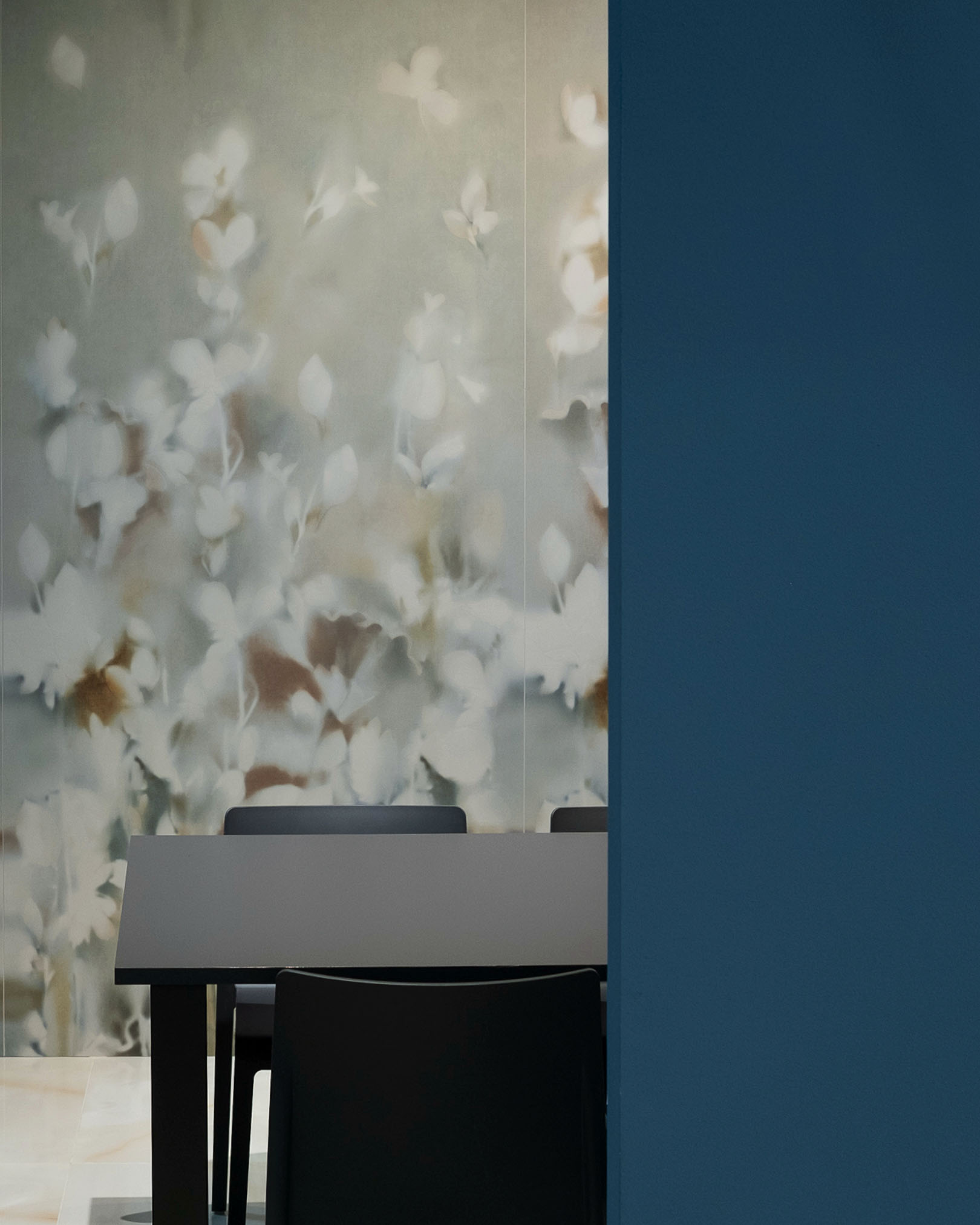 Floral wall in neutral shades behind a matt black table and dark chairs, accented by a contrasting blue wall.