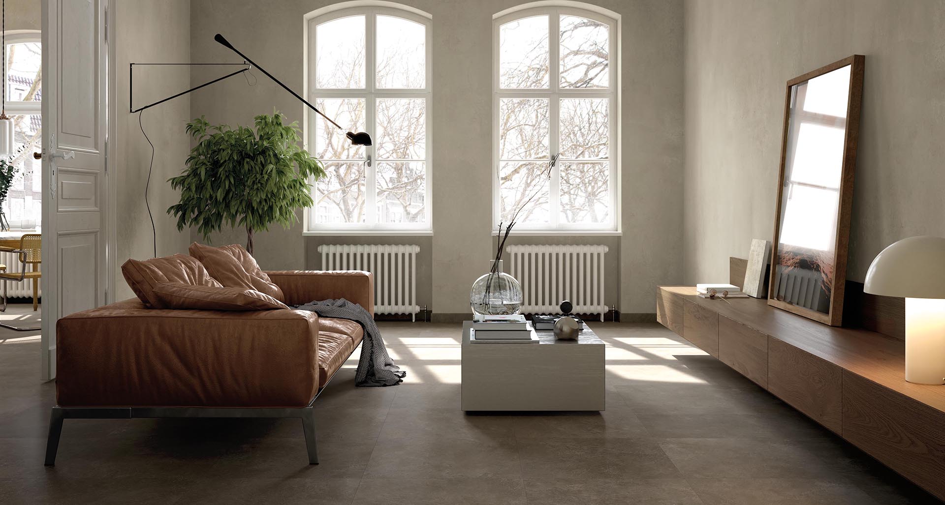 Living room with brown stone effect floor, leather sofa, wooden furniture, lit by large arched windows.