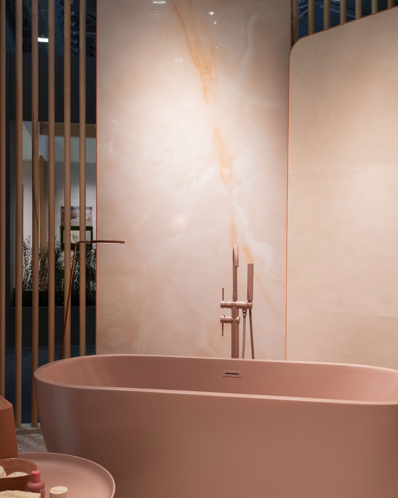 Matt pink freestanding bathtub with beige-pink onyx-effect stoneware wall, matching taps and wooden details.