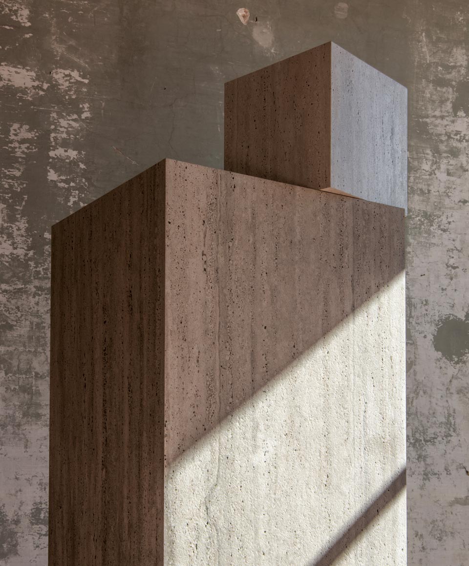 Beige and brown travertine-effect ceramic blocks, illuminated by natural light on a textured gray wall.