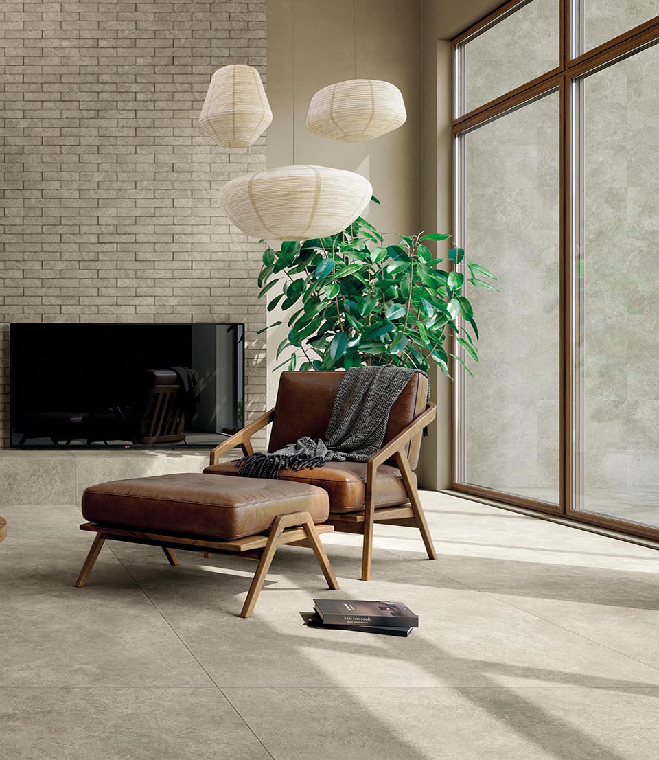 Bright living room with grey stone effect floor, cognac leather furniture, brick wall and large windows with wooden frames.