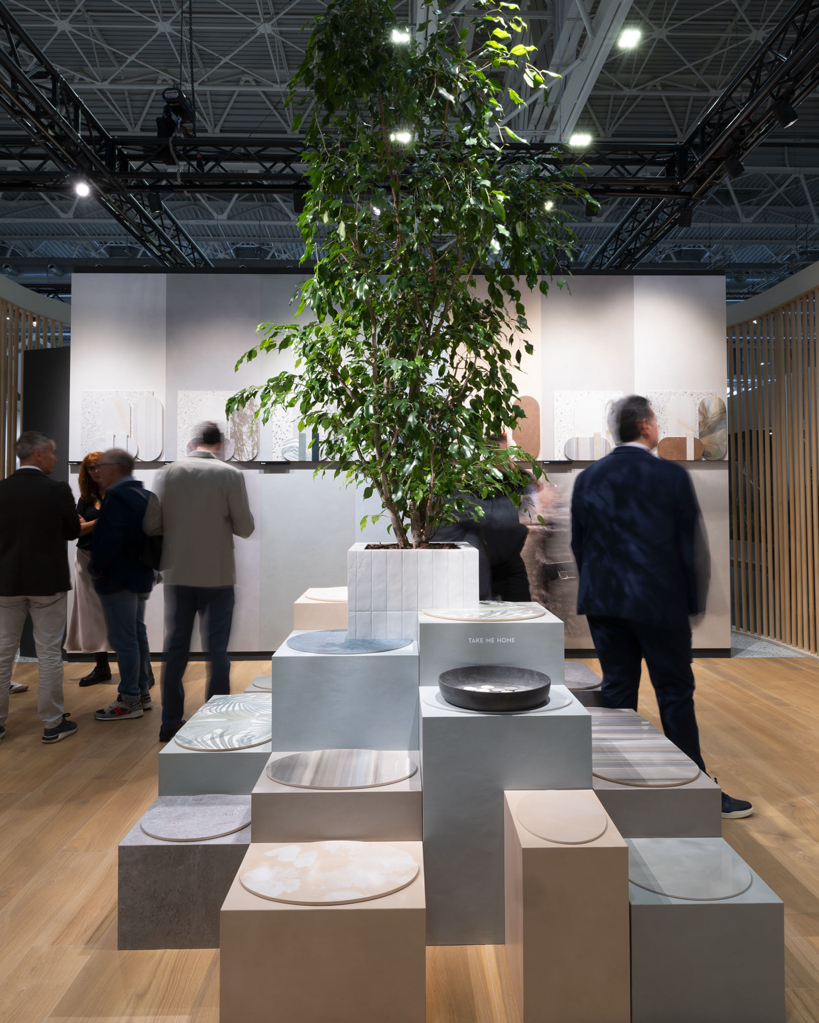 Display with stone-effect ceramic platforms, wood and graphic decorations, with a striking tree in a white pot in the centre.