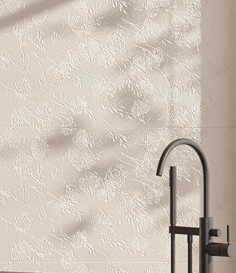 Stoneware wall tiles with floral relief and textural finish and matte black faucet in foreground.