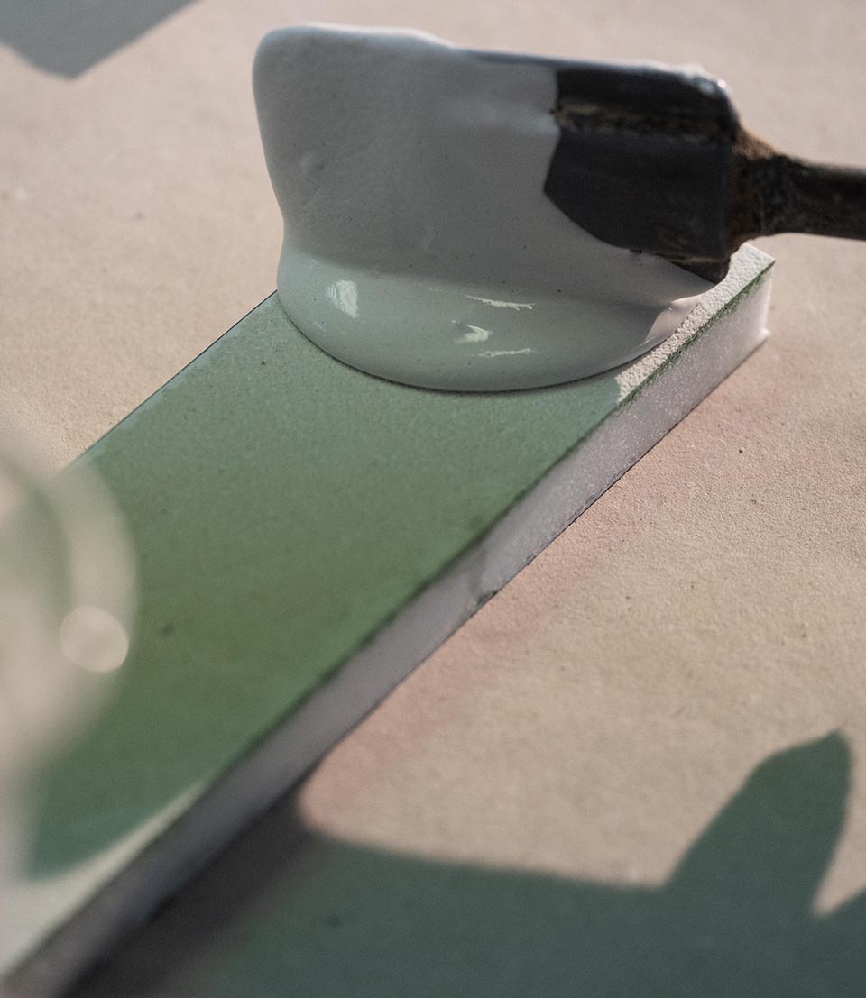 Hand application of white ceramic glaze on green tile, for color and texture testing during craftsmanship.