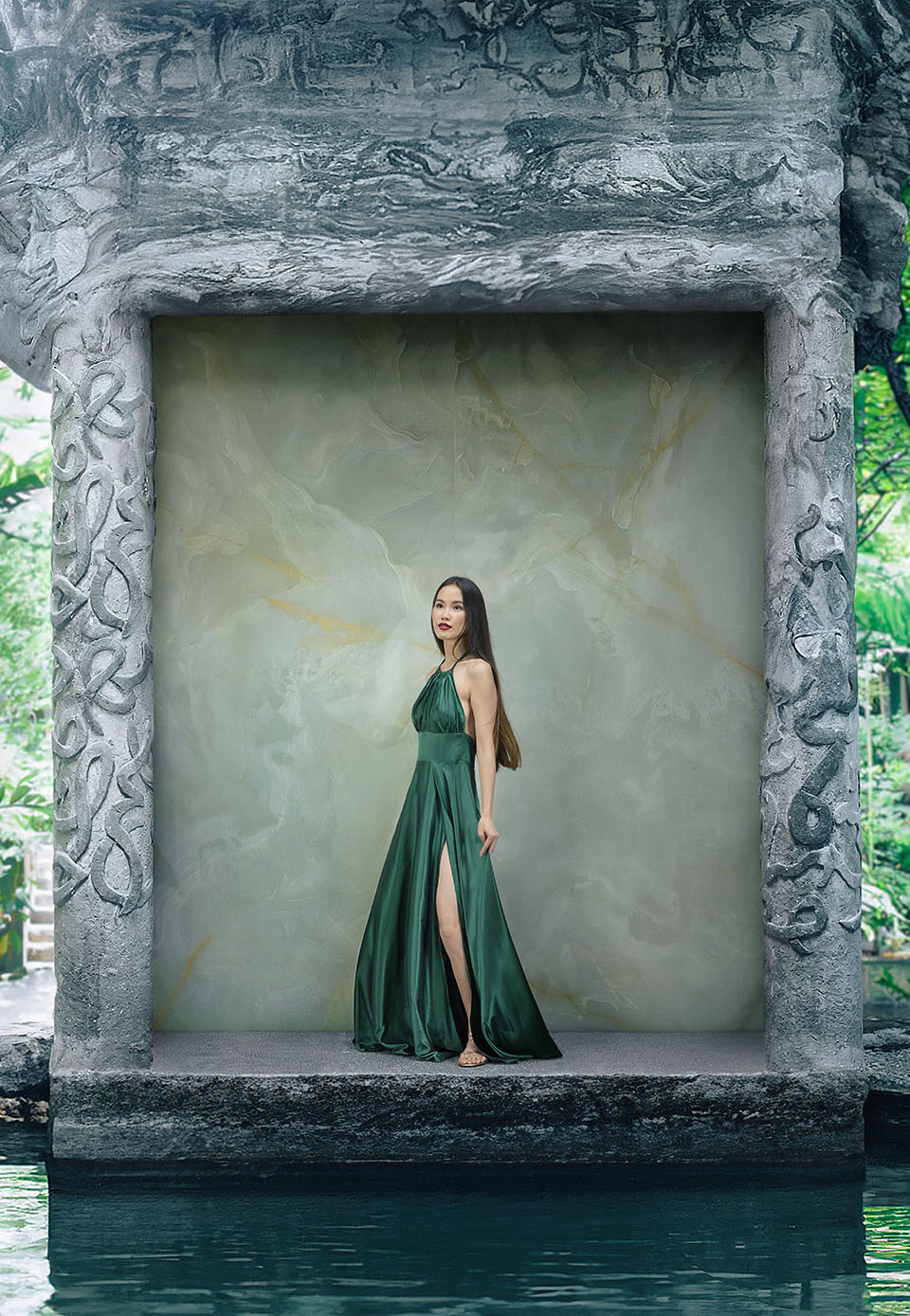 Green onyx-effect stoneware wall with gold veins, carved stone frame and woman in an emerald green dress in front of a swimming pool.