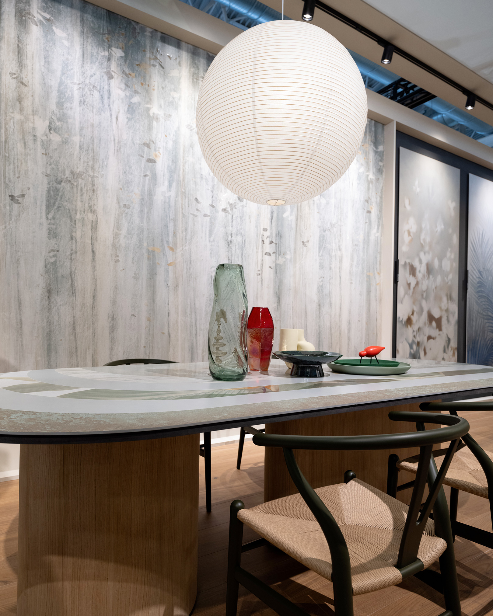 Wooden table with decorative top and woven rope chairs, suspended sphere lamp and textured wall coverings.