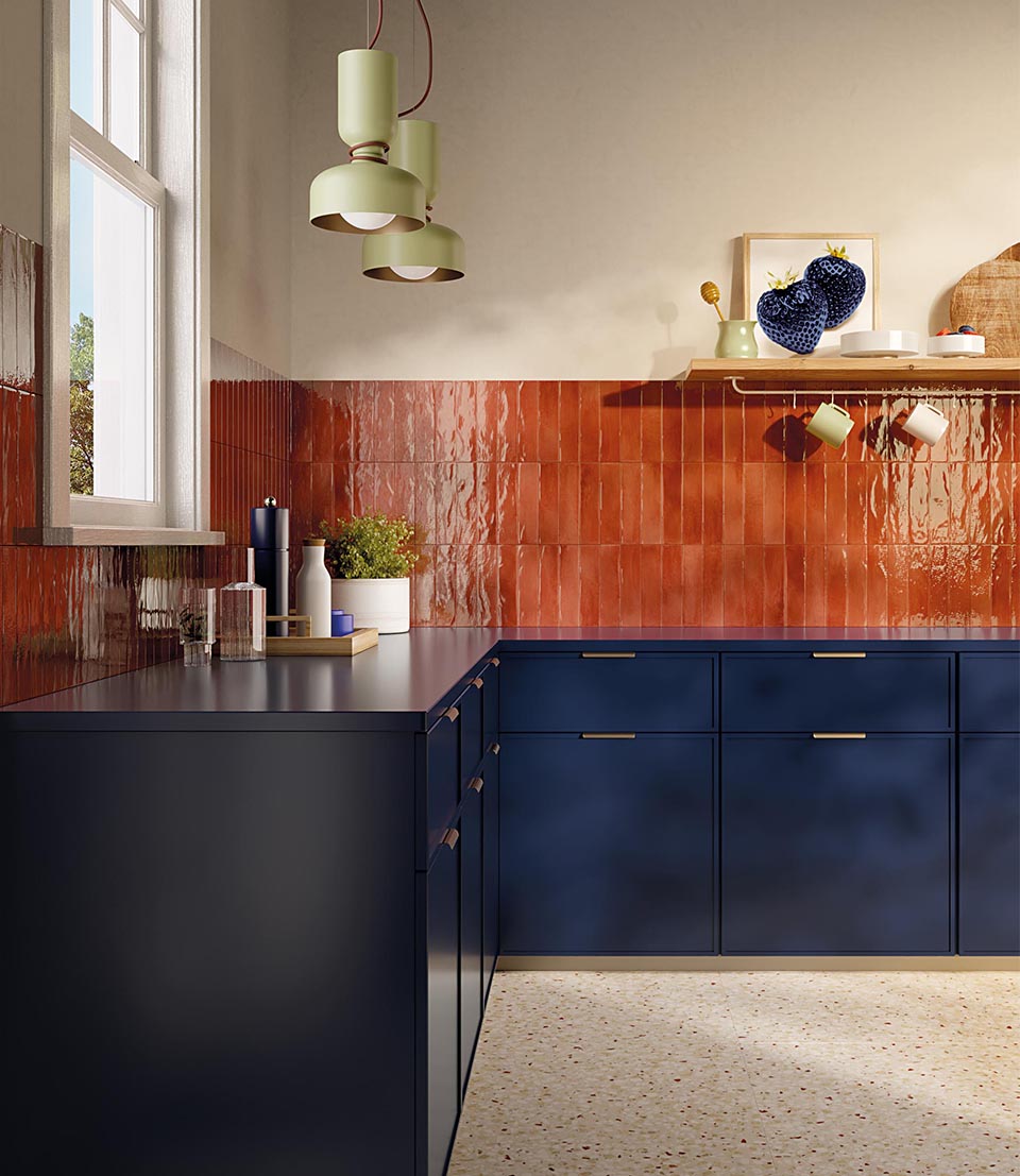 Kitchen with glossy red ceramic wall tiles, matt blue wall units and light terrazzo effect floor, hanging lamps.
