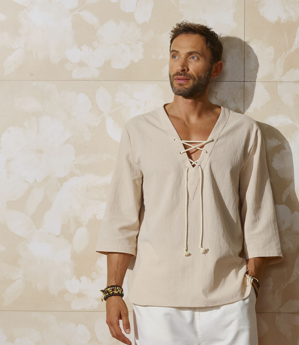 Beige ceramic panels with tone-on-tone floral decoration, man in a light-coloured shirt that enhances the textured and luminous effect of the wall.