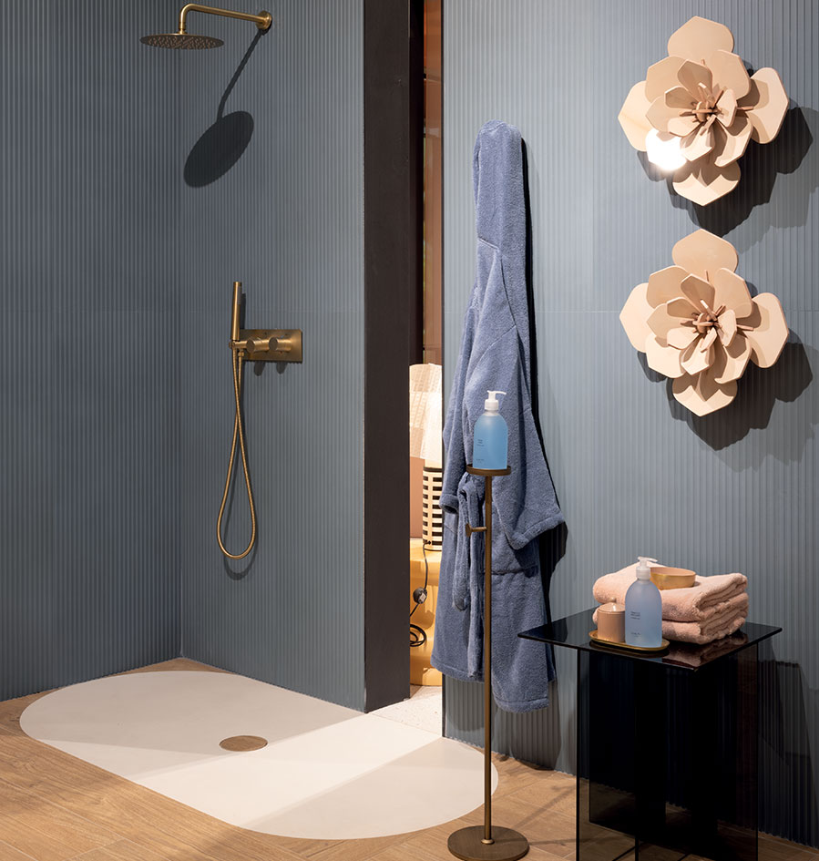 Shower with matt blue vertical slatted cladding, white shower tray, satin gold taps and beige floral decorations.