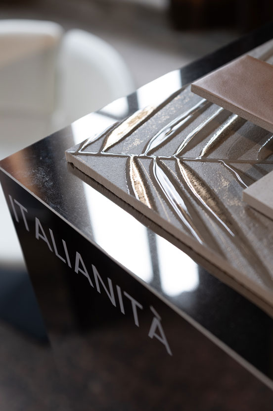 Campione ceramico decorativo con rilievi e riflessi dorati su basamento specchiato con scritta Italianità in evidenza.