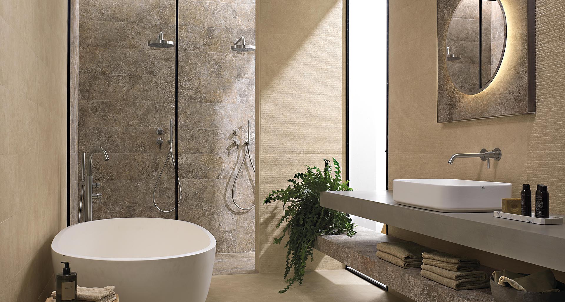Modern bathroom with beige and brown stone effect stoneware walls and floor, double walk-in shower and modern washbasin on suspended top.