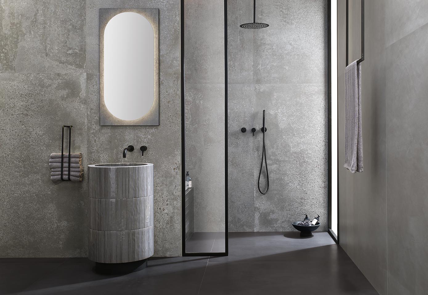 Modern bathroom with cylindrical stone effect stoneware washbasin, concrete grey walls and walk-in shower with matt black details.