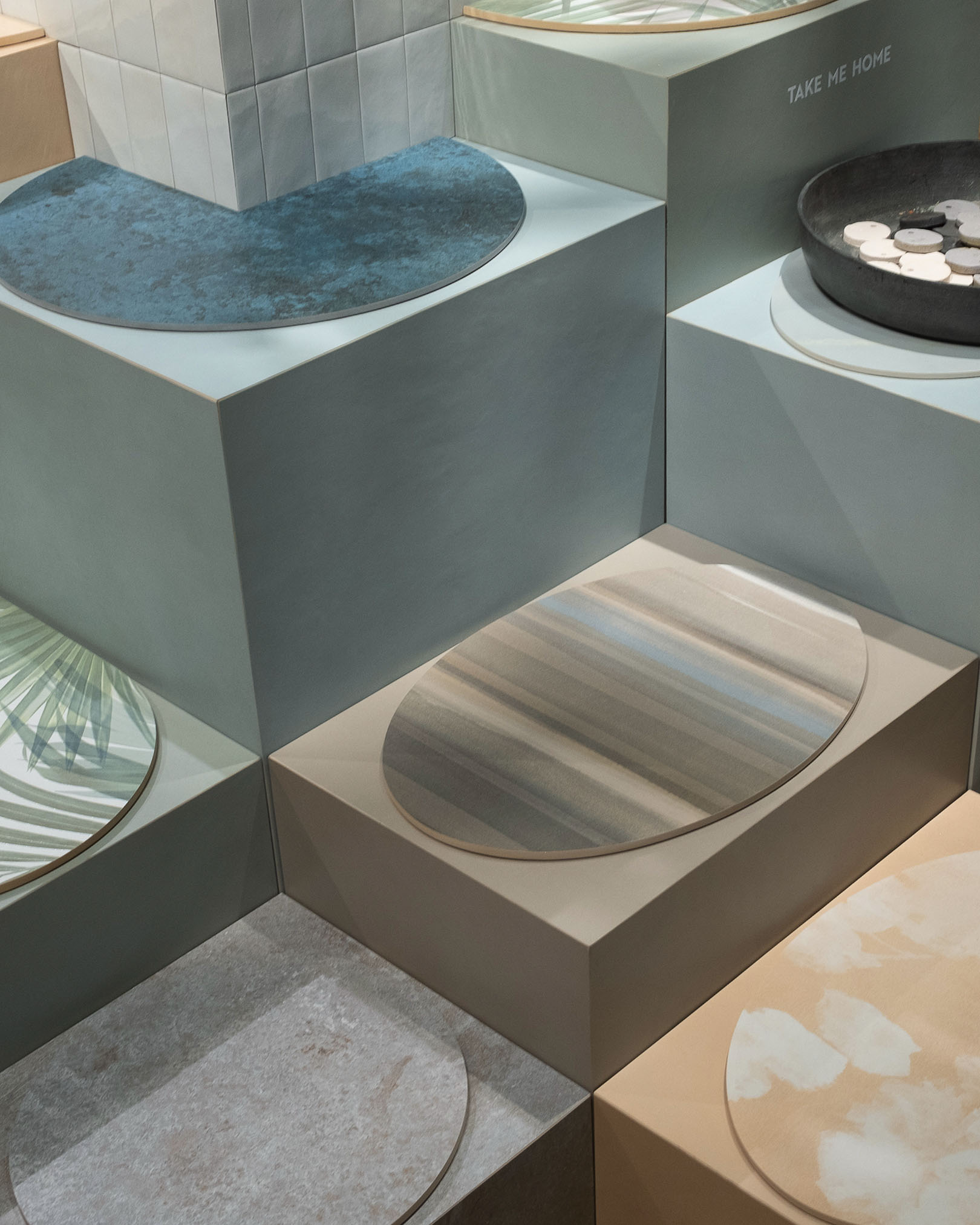 Display of coloured and decorative ceramic slabs, stone and wood effect textures and graphic patterns on geometric platforms.