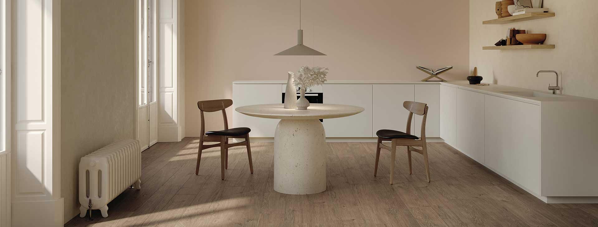 Cucina minimal con pavimento effetto legno naturale, arredi bianchi opachi, tavolo rotondo in pietra e sedie in legno con seduta scura.