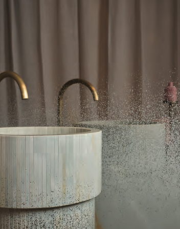 Cylindrical ceramic washbasin with glossy vertical texture, shaded details and satin gold tap on a neutral background.