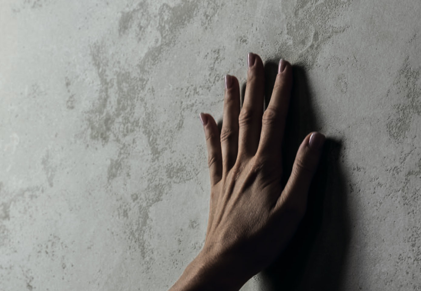 Light stone effect texture with a slightly textured, natural surface, touched by one hand to enhance the sensory experience.