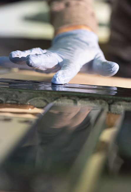Technician applying liquid glaze to tile with blue glove, artisan quality control.