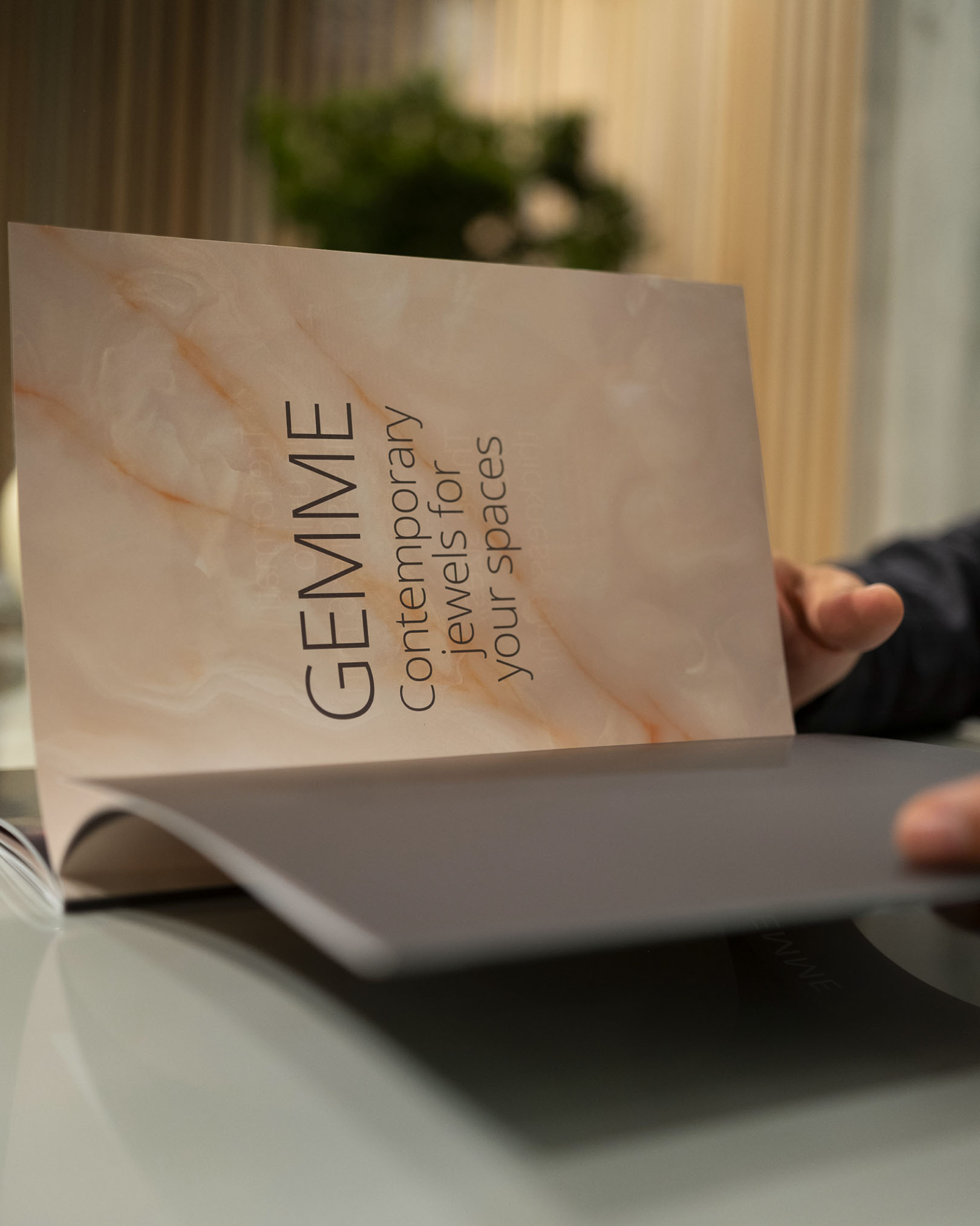 FAP catalogue with beige onyx-effect cover and the word ‘Gemme’ on a satin-finish glass table in a modern setting.