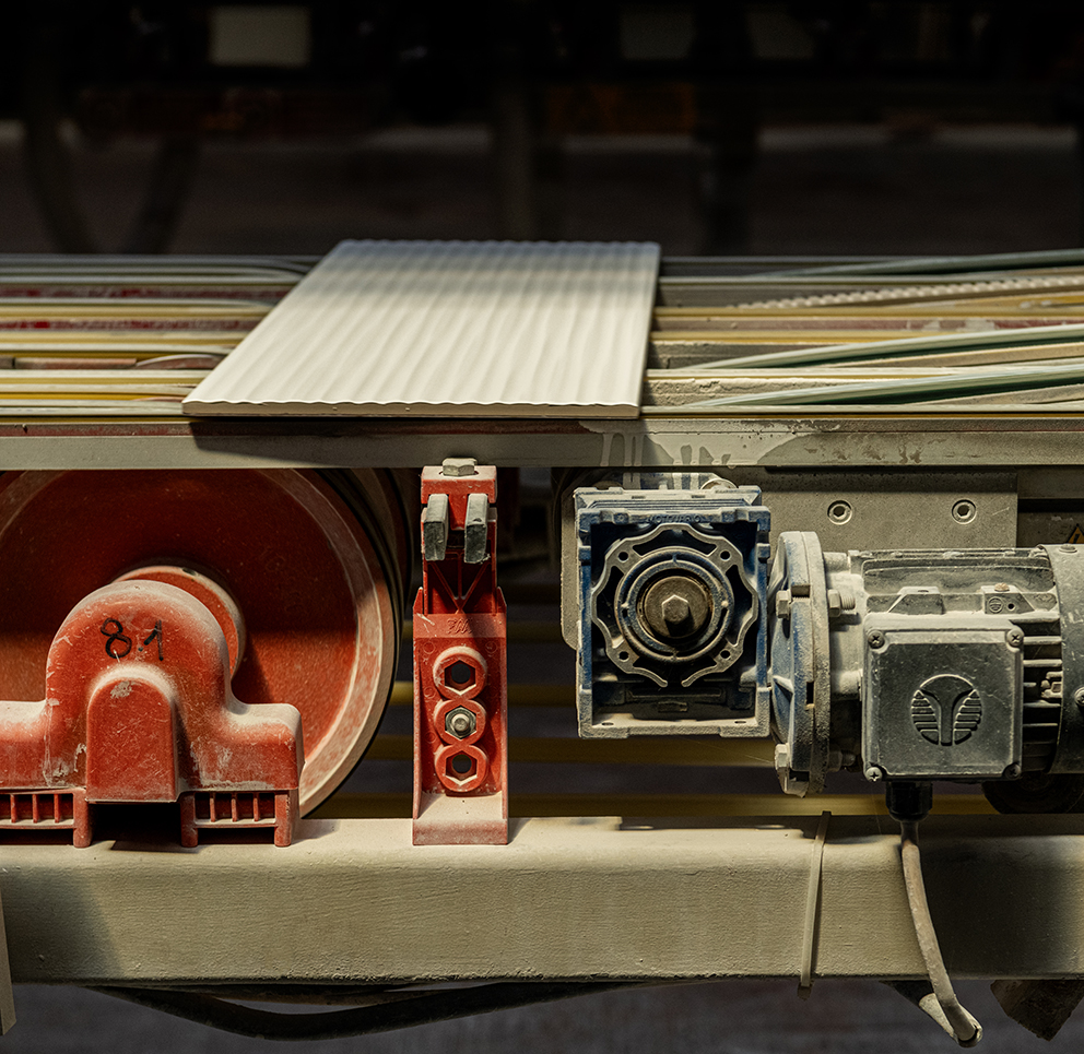 Ceramic production line with white textured tiles on red and blue industrial rollers.
