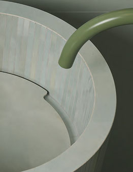 Detail of freestanding washbasin in light grooved ceramic with curved green tap on a monochrome background.