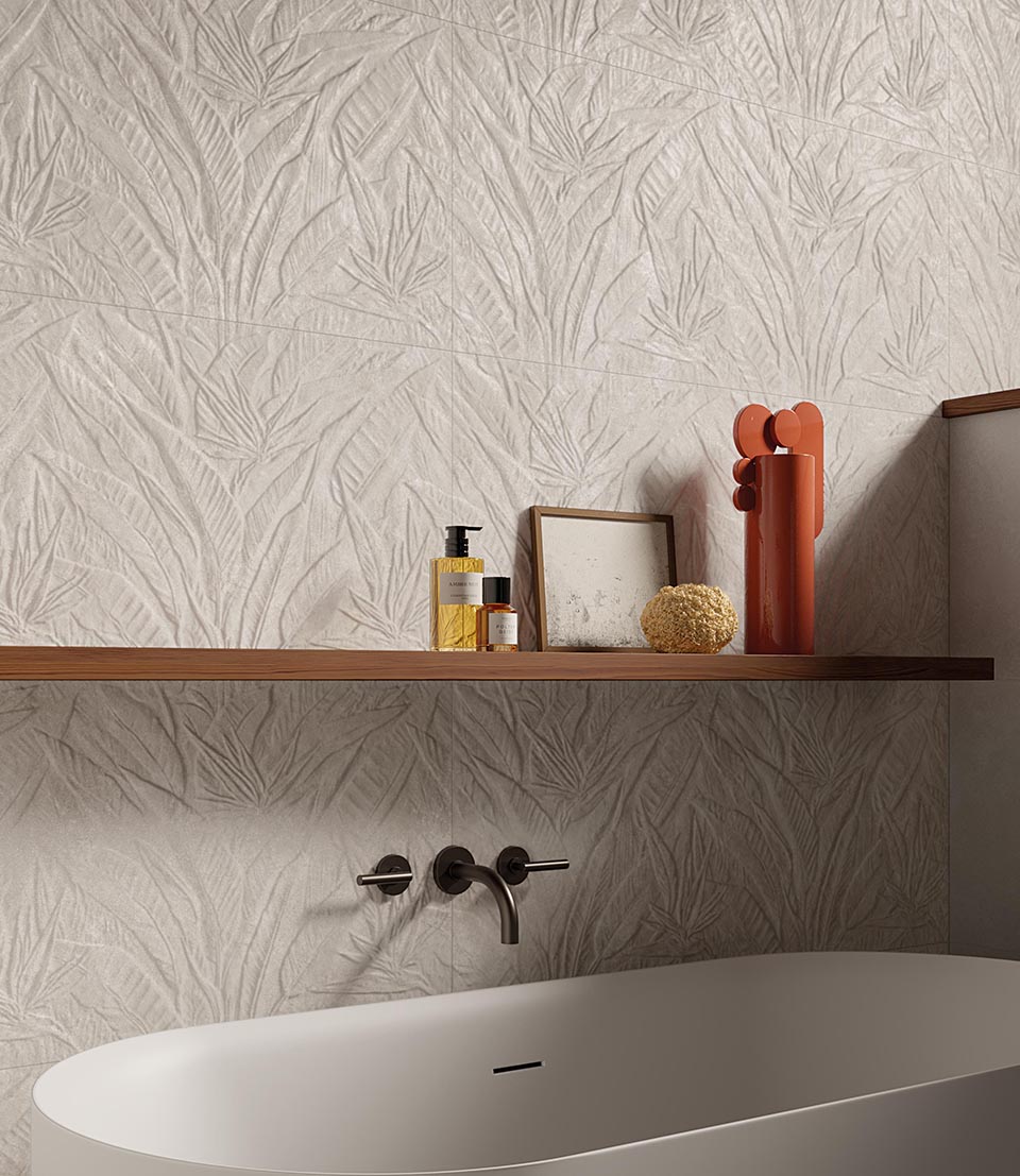 Bathroom cladding with beige stone effect tiles and three-dimensional botanical decoration, combined with bathtub and wooden shelf with cosmetics resting on it.