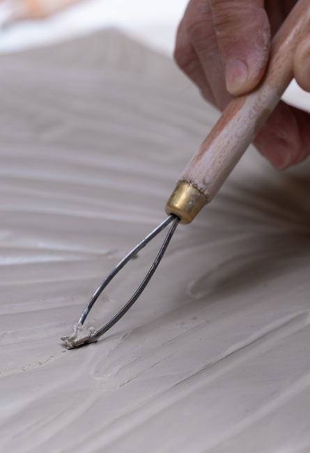 Sculpting of the material with an engraving tool on raw clay, creation of ceramic texture.