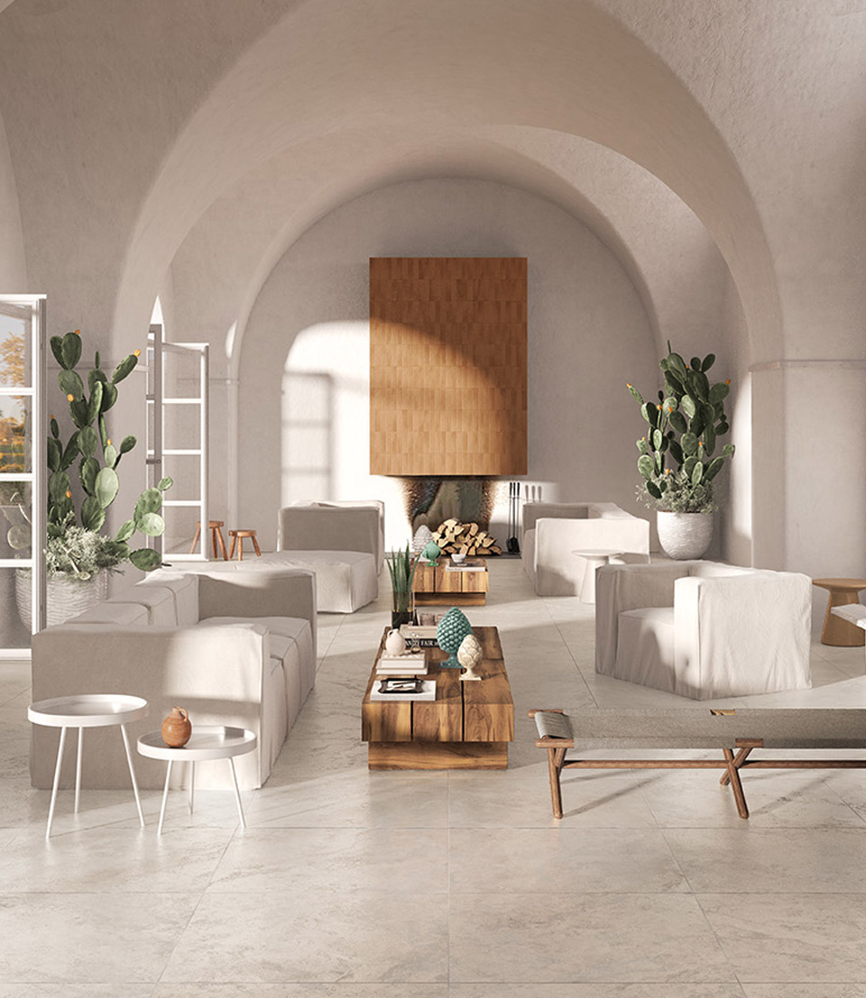 Living room with light stone effect floor tiles, white arches, natural wood furniture, light fabric sofas and armchairs, ornamental plants.