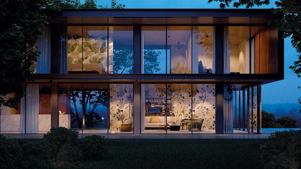 Glass façade of a contemporary house with interiors decorated with tropical tiles illuminated at sunset.