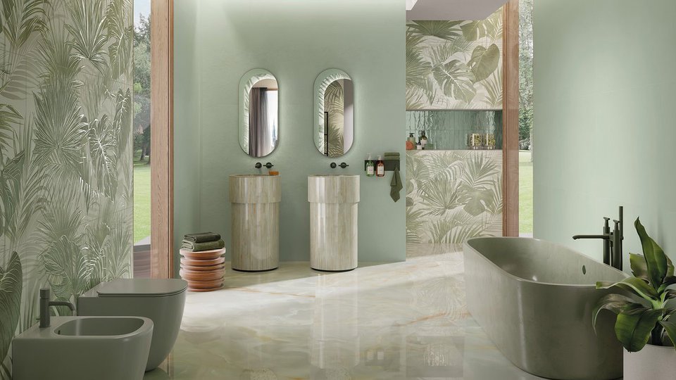Sage green bathroom with glossy tiles and tropical decor, double cylindrical sink and freestanding resin-effect bathtub.