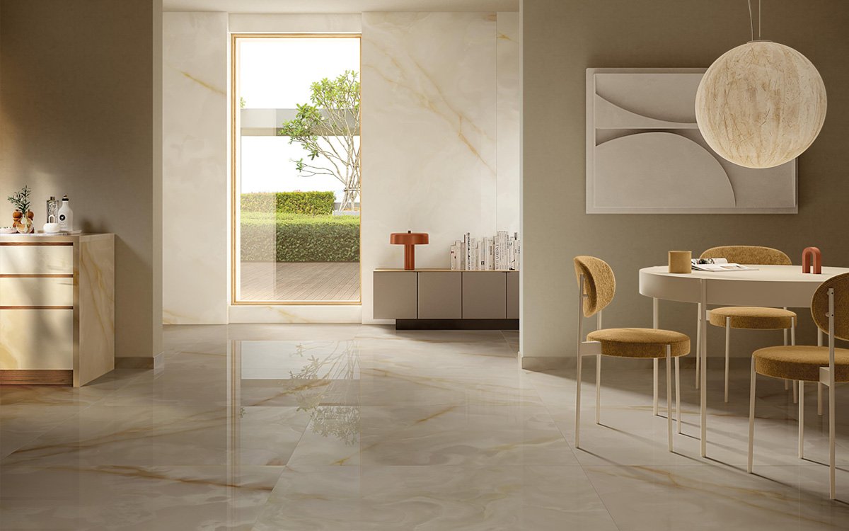 Living area with light marble-effect flooring and beige and ochre furnishings, illuminated by large windows and natural light.