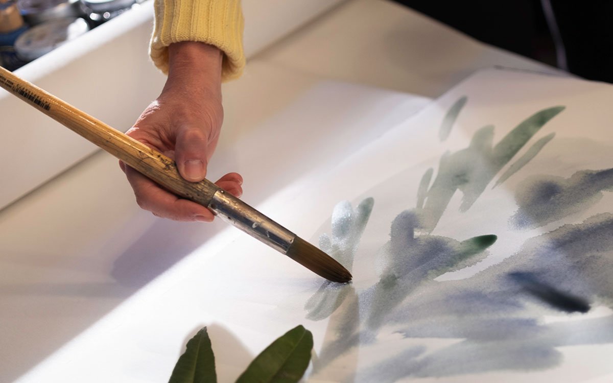 Hand painting with a brush on watercolour paper, artistic creation of natural motifs in shades of green and blue.