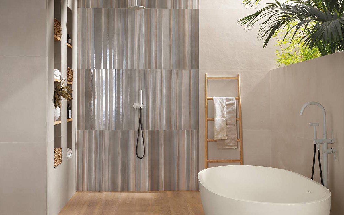 Bagno contemporaneo con pareti beige e rivestimento doccia lucido a righe, pavimento effetto legno e vasca bianca.