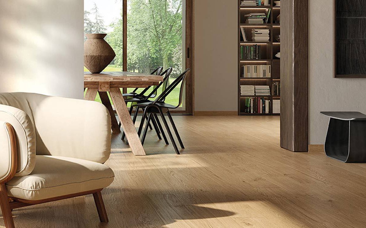 Living naturale con pavimento effetto legno chiaro, arredi in legno massello e ampie vetrate con vista sul giardi