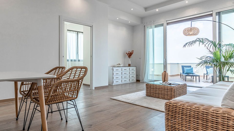 Soggiorno luminoso con pavimento effetto legno, arredi in rattan e vista terrazza arredata con chaise longue.