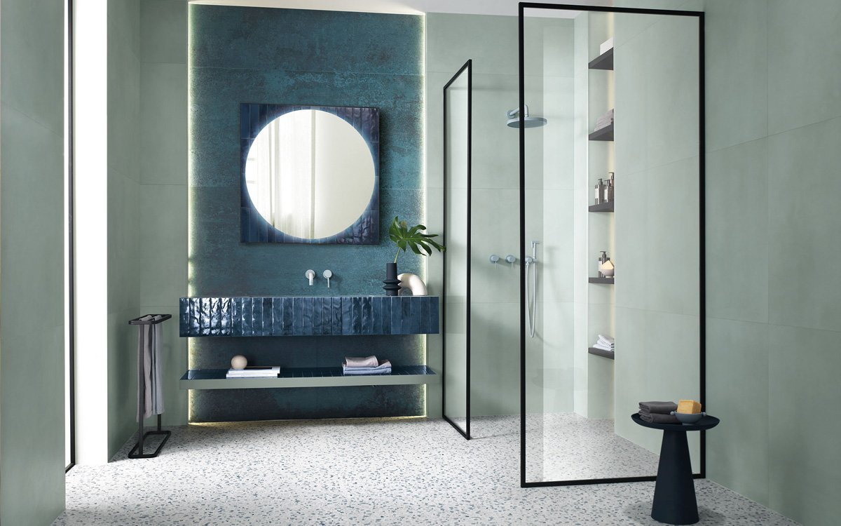 Contemporary bathroom with sage green tiles and glossy blue sink, black details and light terrazzo flooring.
