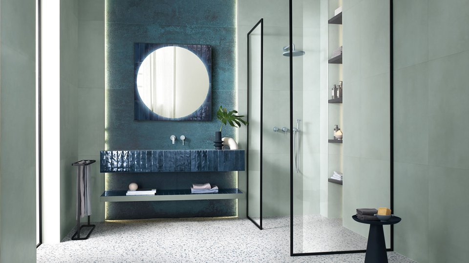 Contemporary bathroom with sage green tiles and glossy blue sink, black details and light terrazzo flooring.