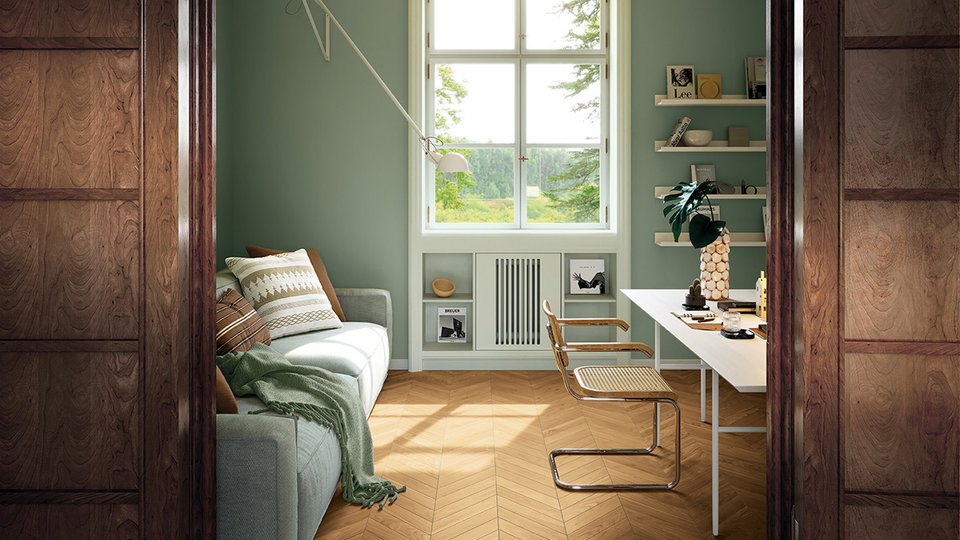 Studio luminoso con pareti verde salvia, pavimento effetto legno a spina di pesce e arredi moderni in legno e metallo.