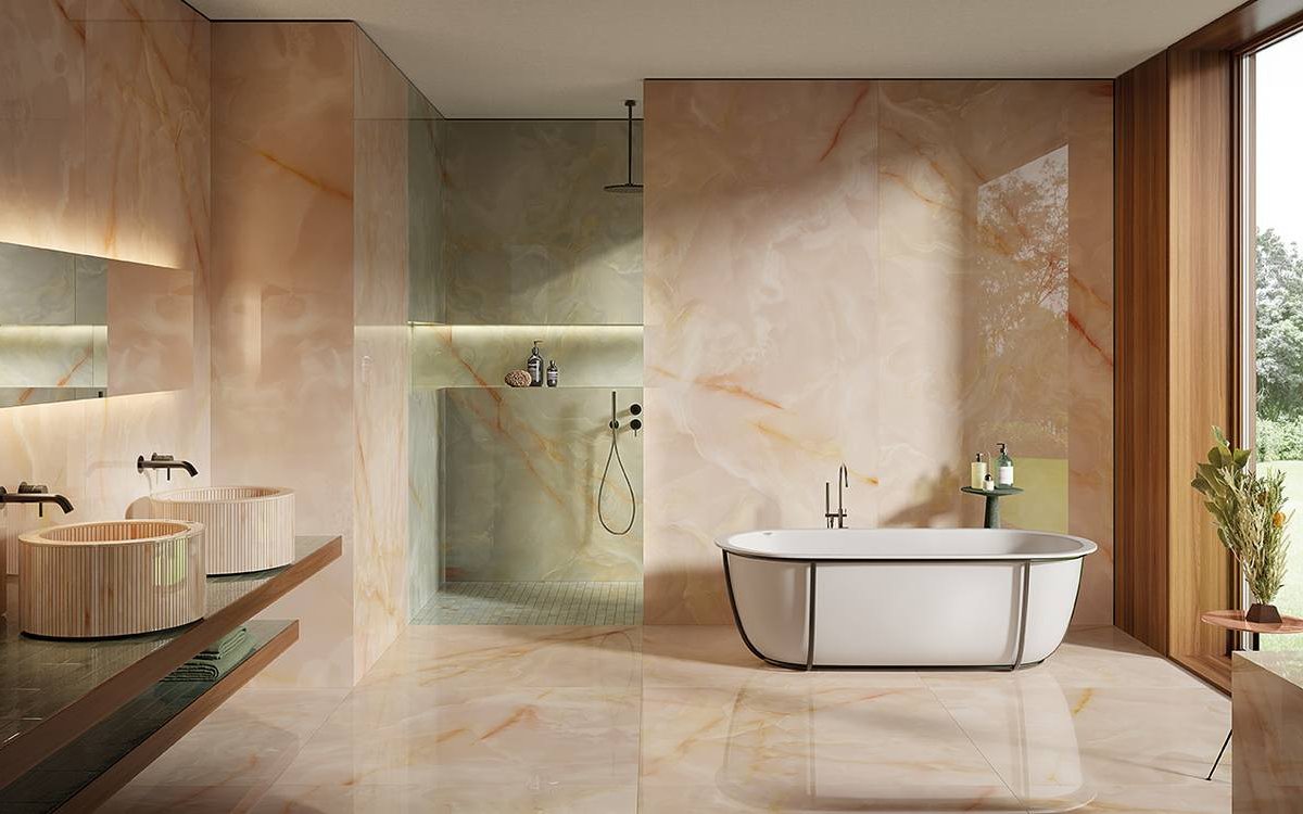 Refined bathroom with glossy pink onyx effect wall tiles, double cylindrical washbasins and white freestanding bathtub.