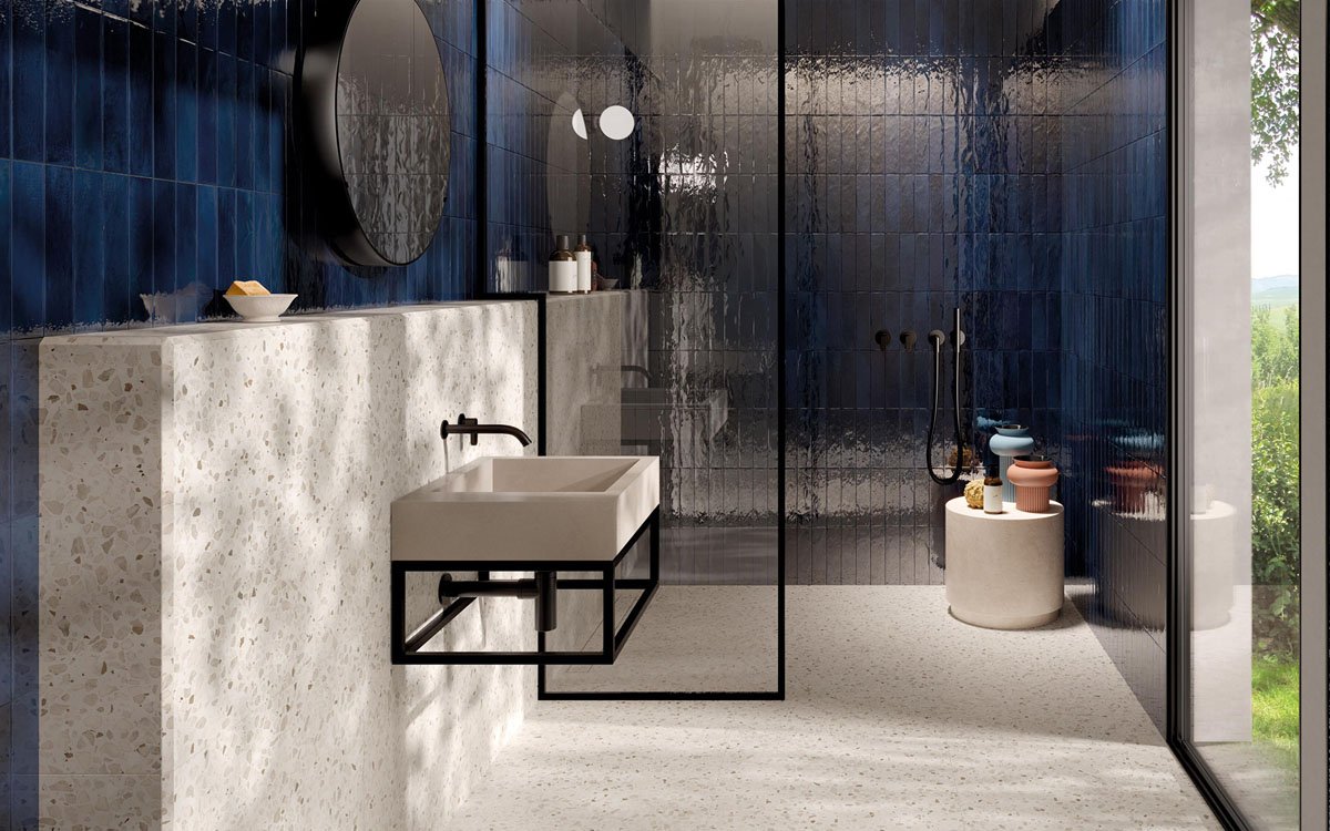 Modern bathroom with deep blue glossy wall tiles, wall-mounted washbasin in light stone and matt black metal details.
